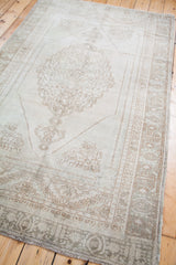 Blanched vintage Oushak rug, lower left corner with medallion, geometric border, and fringe.