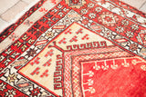 Vintage Turkish prayer rug corner with deep rust, cream geometric patterns, and fringe.