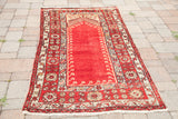 Deeply saturated rust mihrab and field with movement motifs, bordered by geometric patterns and fringe.