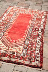 Vintage Turkish prayer rug corner, showing rust and cream geometric patterns and fringe.