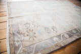 Muted gray border and light fringe on a vintage Oushak rug with pastel floral motifs.