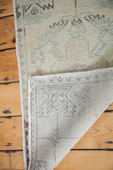 Folded vintage Oushak rug displaying hand-knotted backing and blanched geometric pattern.