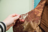 Delicate floral lace detail on the brown 1940s gown sleeve with minor separation.