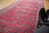 Angled view of the vintage Meshed runner showing its raspberry red field and repeating floral motifs.