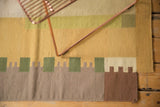 Secured bottom edge of contemporary Kilim carpet with beige, green, and brown geometric blocks.