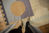 Contemporary Kilim with abstract circles, geometric blocks, beige, slate, violet, viewed with feet.