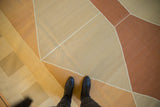 Modern geometric kilim in pale copper, gold, beige, with crisp white lines and black boots.