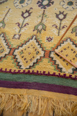 Detail of a vintage Moroccan rug's full saffron pile, purple border, and soft yellow fringe.