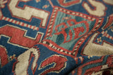 Folded antique Kazak rug showing hand-knotted texture in sapphire blue, brick red, and oxidized green.