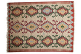 Vintage Turkish Kilim carpet features repeating rams horn geometric medallions in ivory, red, green, and blue.