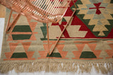 Serrated geometric border with natural fringe on a vintage Turkish Kilim in peach, green, ivory.