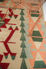 Close-up of hand woven Kilim with serrated geometric patterns in cherry red, green, ivory, peach, and blue.
