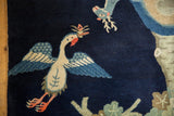 Beige bird holding an offering, with blue wings on dark indigo vintage Peking rug.