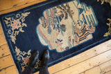 Antique Peking rug runner from an angle, displaying the pictorial village scene and dark blue border.