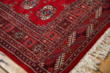 Intricate cherry red, navy, ivory patterns and fringe on a vintage Bokhara rug corner.