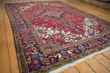 Navy blue Heriz border, geometric floral motifs, cherry red field, and ivory fringe.