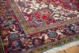 Vintage Heriz carpet corner: geometric floral border in cherry red, navy, and gold, with ivory fringe.