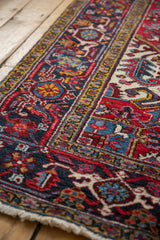 Vintage Heriz carpet corner showcasing rich red, navy, gold geometric motifs and ivory fringe.