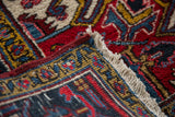 Close-up of vintage Heriz carpet's thick pile, white fringe, red selvage, and geometric red, blue, gold pattern.