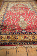 Lush pile of a cherry red vintage rug with a central floral urn and multi-layered borders.