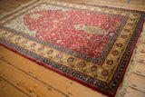 Angled view of a vintage Romanian Hereke rug showing its full pile, red field, and golden floral border.