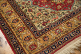 Corner of a vintage Hereke design rug showing the sand and blue floral borders and ivory fringe.