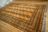 Full view of a vintage Afghani Daulatabad carpet showing its saffron yellow field and rows of dark navy guls.