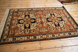 Angled view of a vintage Romanian Kazak rug with geometric starburst medallions and borders.