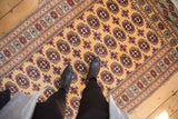 Repeating elephant footprint guls in red and black on the golden pile of a Bokhara rug.