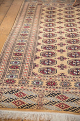Angled view of a vintage Bokhara rug highlighting the intricate geometric border and plush, even pile.