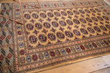 The lush, even pile and intricate borders of a vintage Pakistani Bokhara rug shown from an angle.