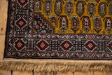 The vintage Romanian rug's corner with raspberry red geometric borders, full pile, and clean fringe.