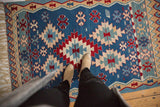 Hand-woven vintage Turkish Kilim rug's geometric medallions and wave patterns in blue, red, sand.