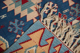 Turkish Kilim rug corner detail: hand woven geometric pattern, blue selvage, cream fringe.