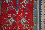 Close-up of the vintage Turkish Kilim's cherry red pictorial field and multicolored striped border.