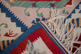 Folded vintage Turkish Kilim rug corner, displaying flatweave, fringe, and red, blue, ivory geometric designs.