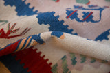 Hand-woven texture of a folded Kilim rug, showing geometric sky blue and cherry red motifs.