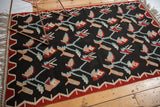Charcoal black Kilim rug with dusty apricot, powder blue plant motifs, red zigzag border.