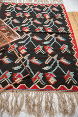 Charcoal Turkish Kilim rug showing colorful germinating plant motifs and natural fringe.