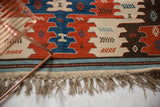 Hand woven Turkish Kilim rug with natural fiber fringe and a striped border in blue, ivory, and red.