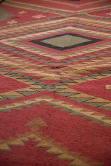 Vintage Indian Soumac carpet close-up, showing serrated geometric patterns in brick red and pale green.