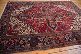 Angled view of the vintage Persian Mehrivan carpet's bold geometric medallion and dark navy border.