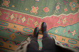 Vintage Dhurrie rug detail showing geometric patterns in dusty green, pale raspberry, turquoise, and sand.