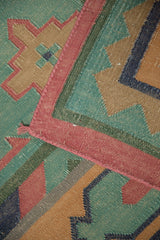 Dhurrie flatweave detail: geometric design with dusty green, pale raspberry, sand, and blue.
