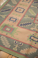 Angled view of hand woven Dhurrie, featuring sage green and apricot geometric patterns.