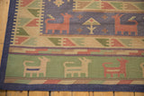 Dhurrie carpet corner, showing seafoam green stylized animal motifs and blue selvage.