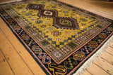Siberian Caucasian carpet's interconnected diamond contour with blooming motifs on dusty gold field.