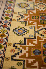 Saffron yellow Kazak runner field, repeating starburst medallions, geometric border with sky blue, copper.