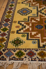 Close-up of full pile saffron yellow field, geometric Kazak motifs, and white fringe.