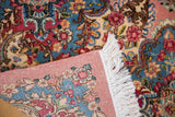 Hand-knotted Kerman carpet corner showing the dusty rose foundation and dense floral pile.